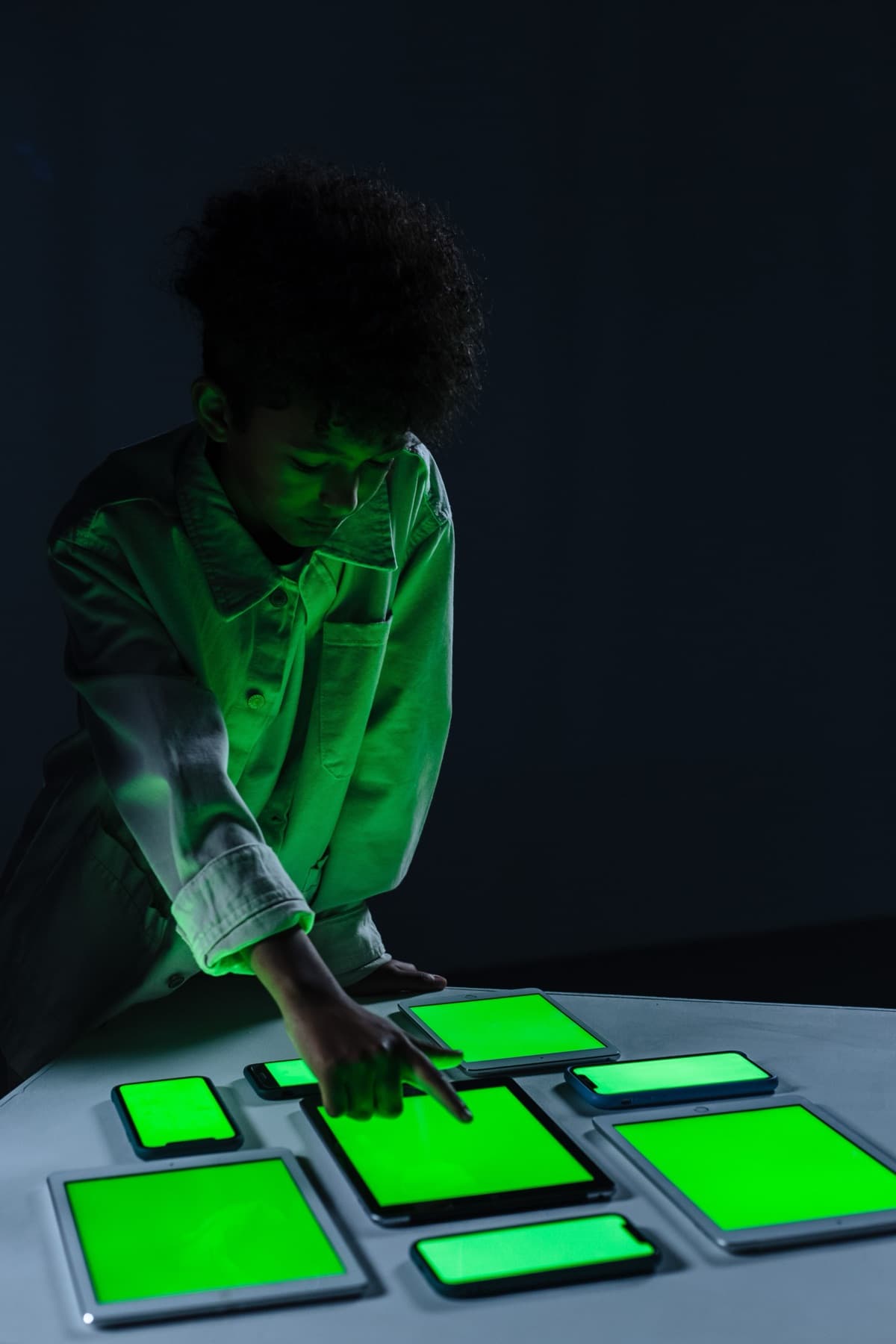 Persona interactuando con tabletas y móviles de pantallas verdes en una sala oscura